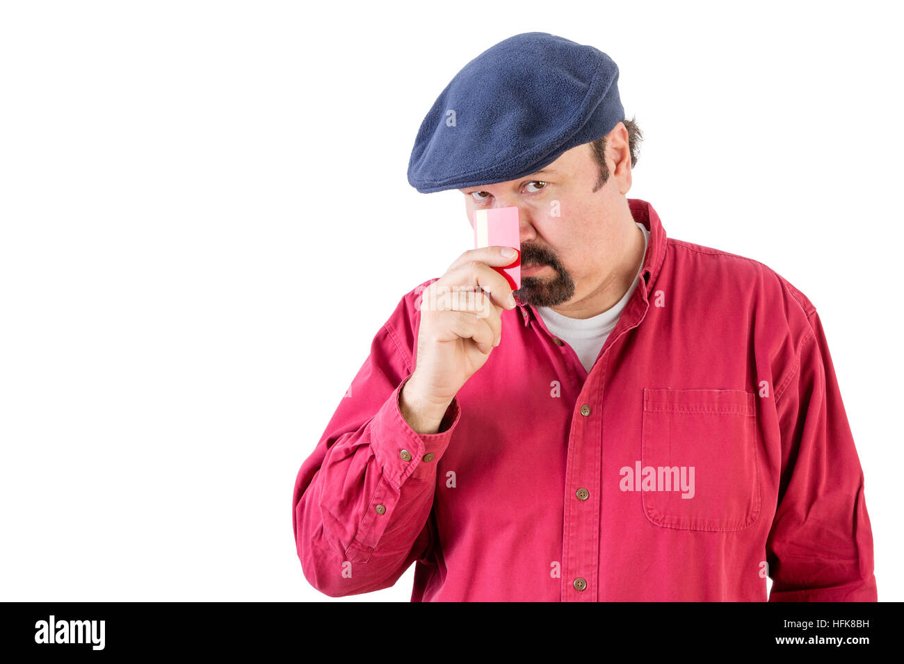 Suspicious middle-aged man wearing a cloth cap peering over his credit card with a speculative watchful expression as he holds it to his nose Stock Photo