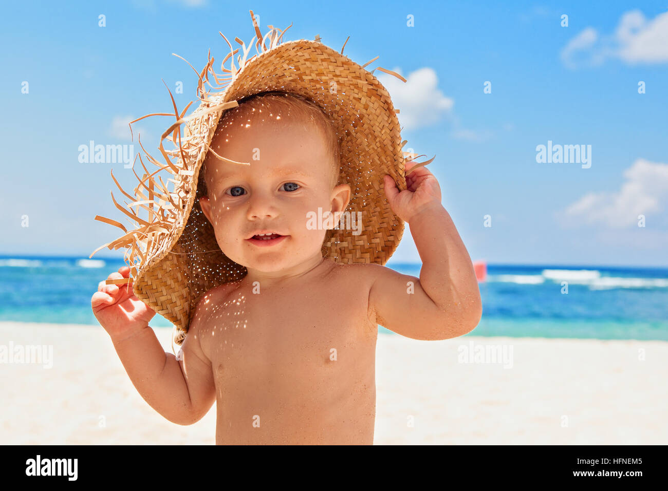 Funny happy baby boy on beach with straw hat, dirty face covered with sand. Family travel, healthy lifestyle, holiday recreation Stock Photo