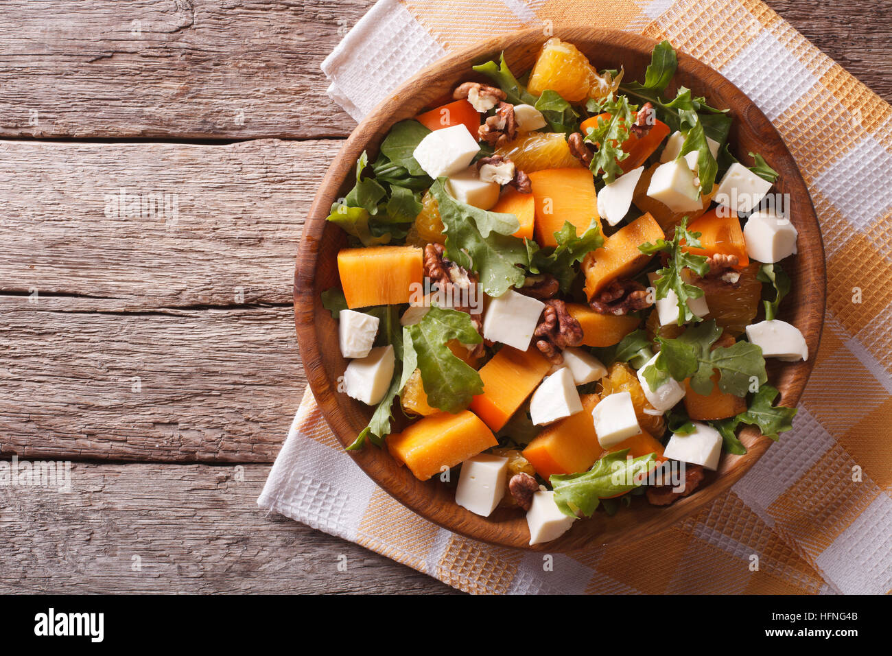 salad with persimmon, arugula, oranges, nuts and cheese on the table. horizontal view from above Stock Photo