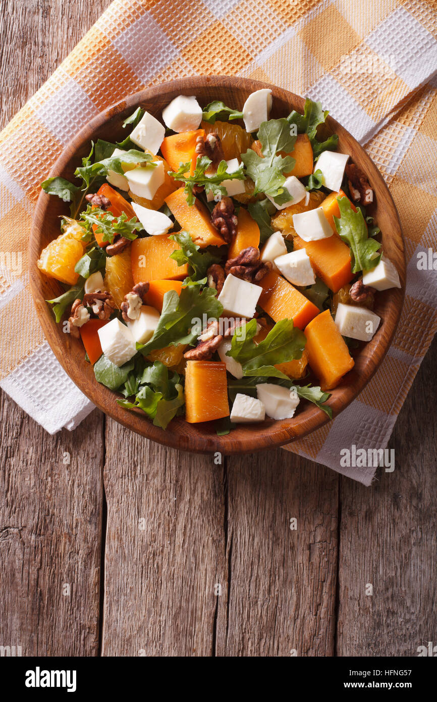 salad with persimmon, arugula, oranges, nuts and cheese on the table. vertical top view Stock Photo
