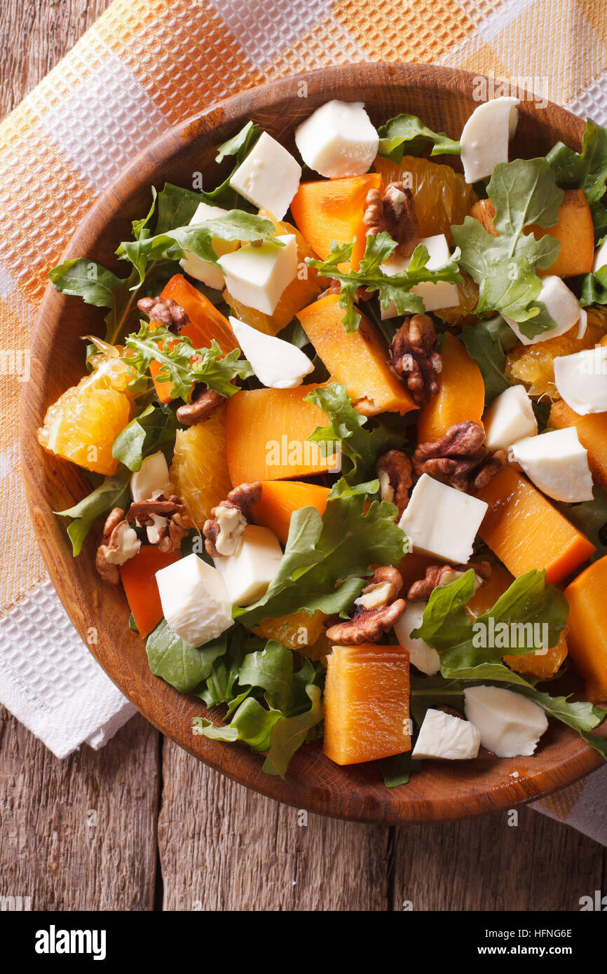 salad with persimmon, arugula, oranges, nuts and cheese close-up on the table. vertical top view Stock Photo