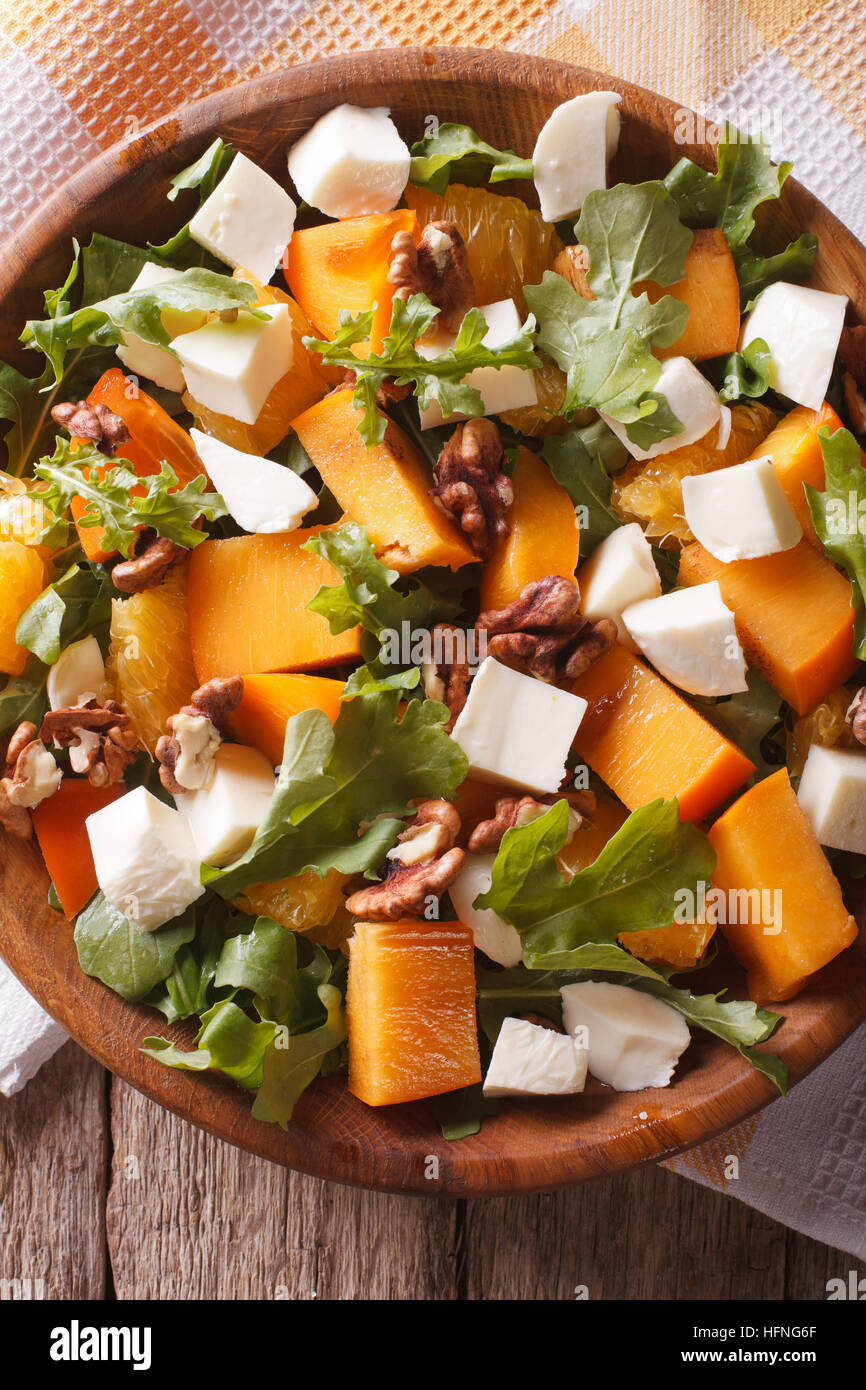 salad with persimmon, arugula, oranges and cheese close-up on the table. vertical top view Stock Photo