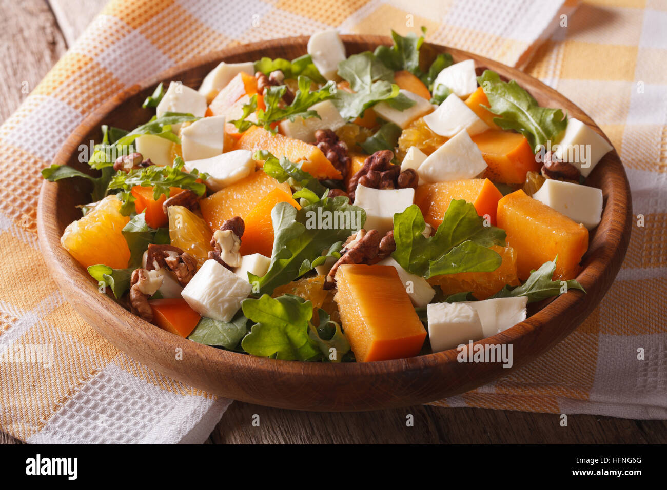 salad with persimmon, arugula, oranges and cheese close-up on the table. Horizontal, rustic Stock Photo