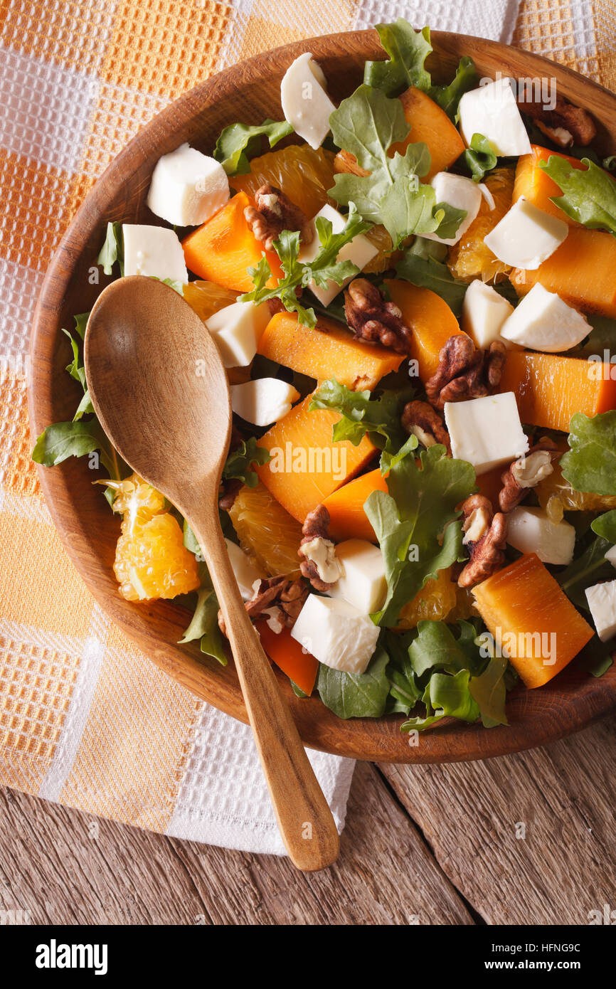 Fresh salad with persimmon, arugula and cheese close-up on the table. vertical top view Stock Photo