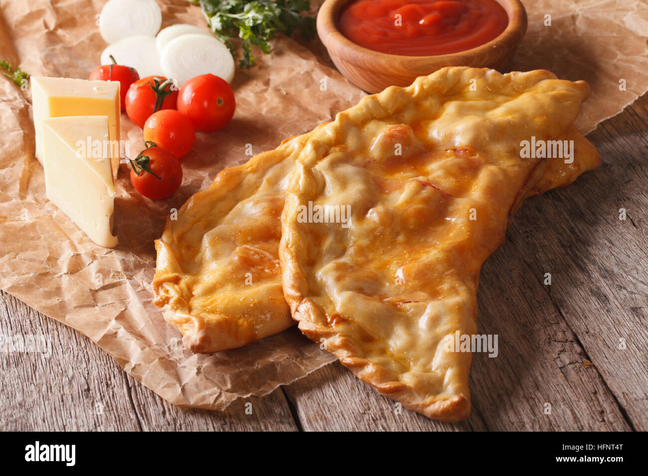 Italian pizza calzone closeup on a paper and ingredients. Horizontal, rustic Stock Photo