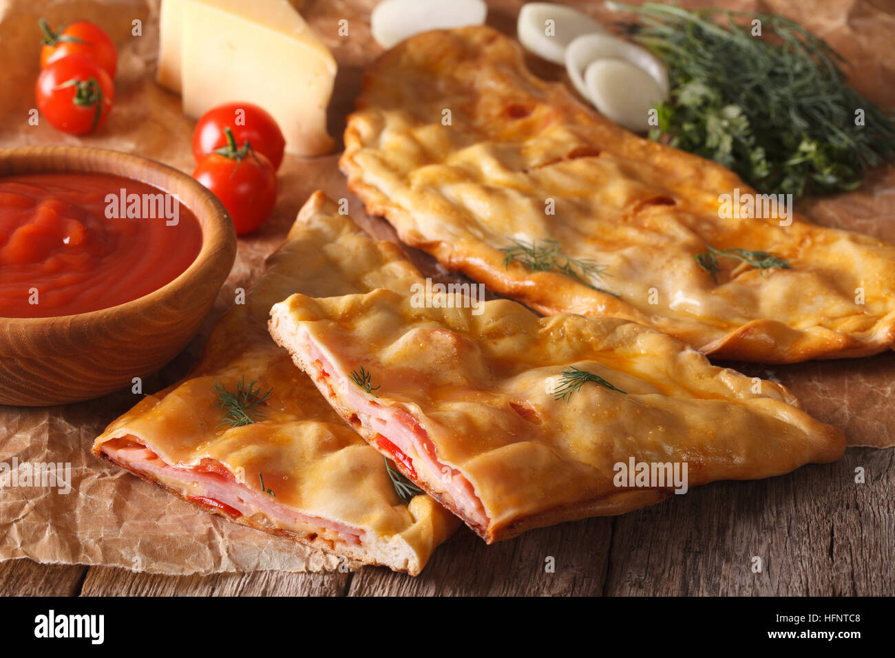 Cut Italian pizza calzone with ham and cheese close-up on the table and ingredients. horizontal Stock Photo