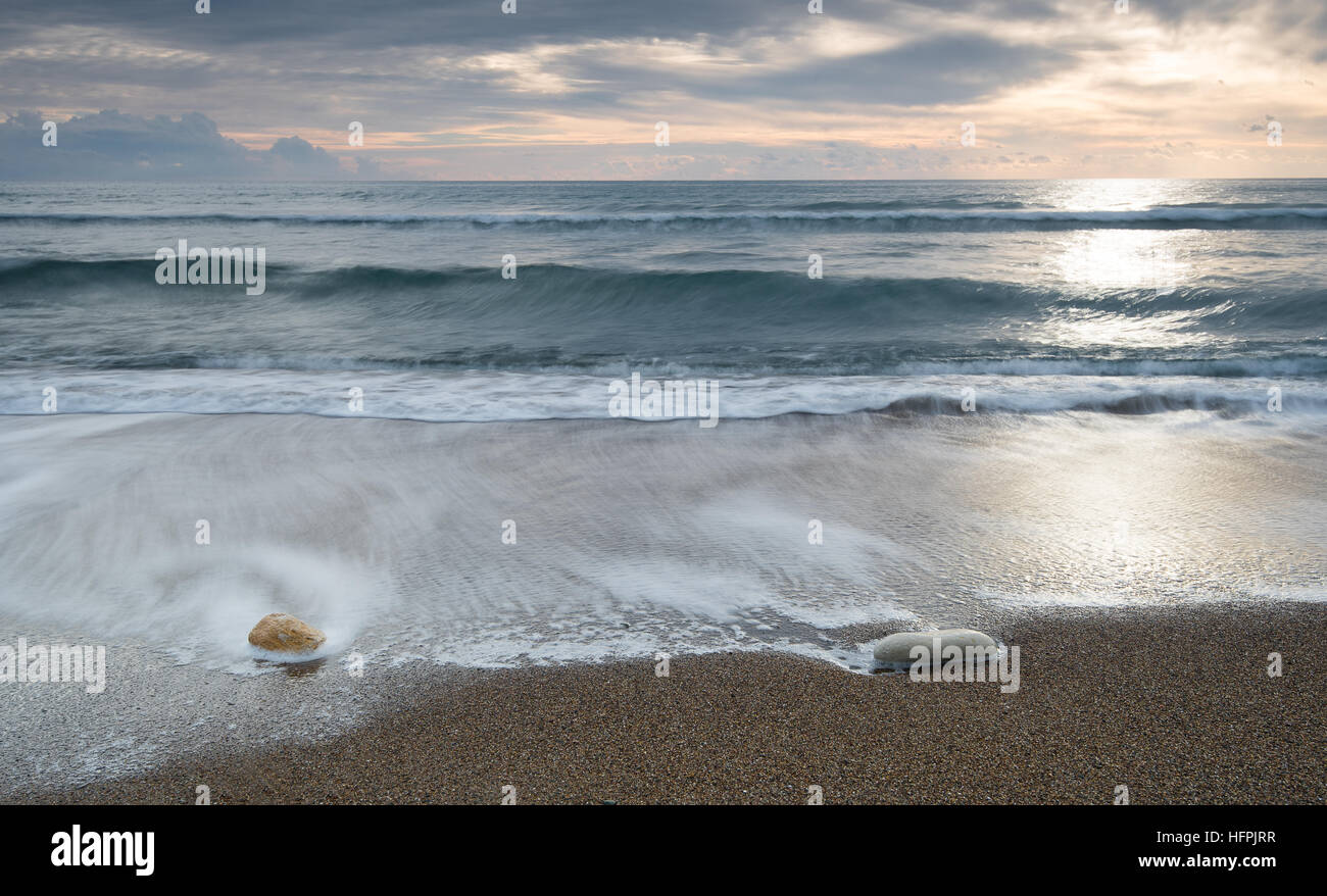 Pebbles on the beach and flowing sea water during sunset creating nice textures. Long exposure image. Stock Photo