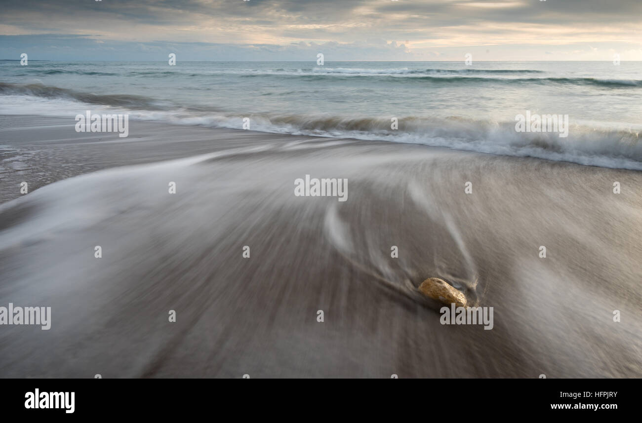 Pebble on the beach on a black sand and flowing sea water creating nice textures. Long exposure image. Stock Photo