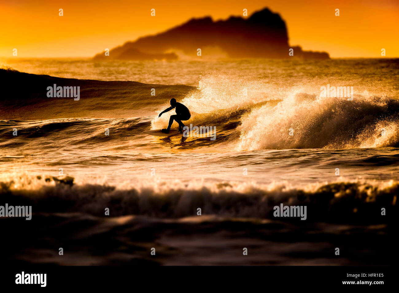 A surfer riding a wave during a golden sunset at Fistral in Newquay, Cornwall.  Surfer in action. UK. Stock Photo