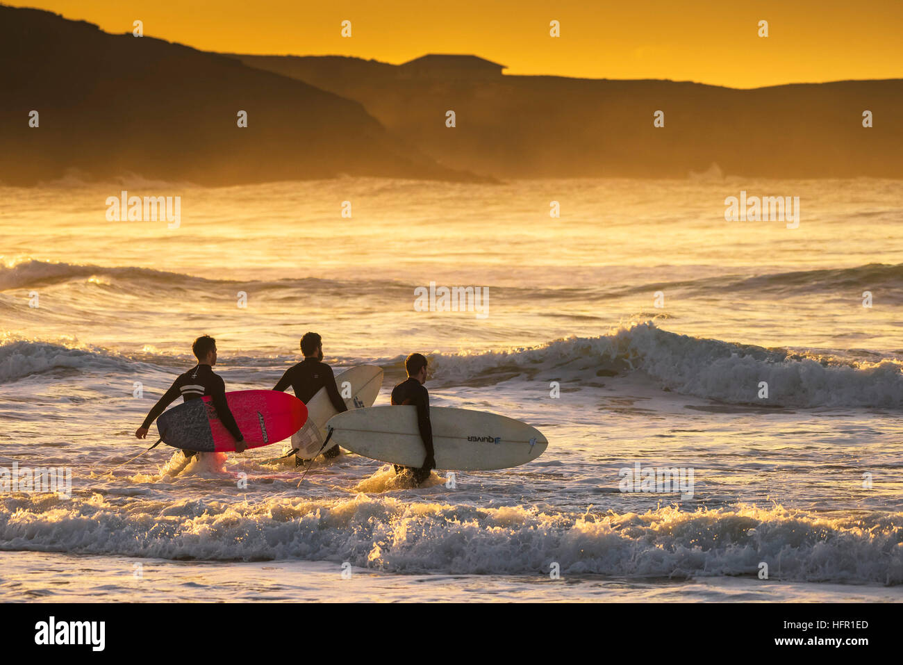 Three surfers walk into the sea at Fistral in Newquay, Cornwall. UK. Stock Photo