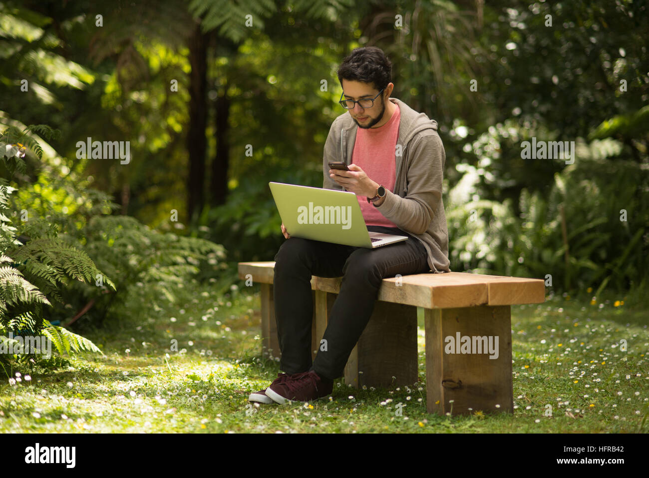 Young man with a laptop and smartphone sitting outdoor in a park Stock Photo