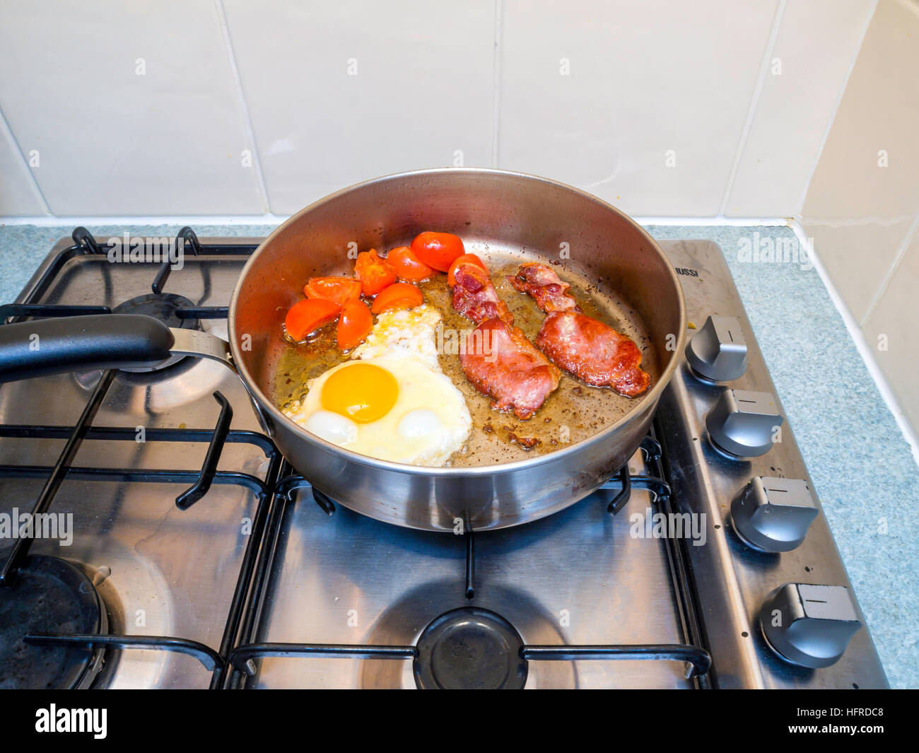 Bacon egg and tomatoes being fried in sunflower oil in stainless steel