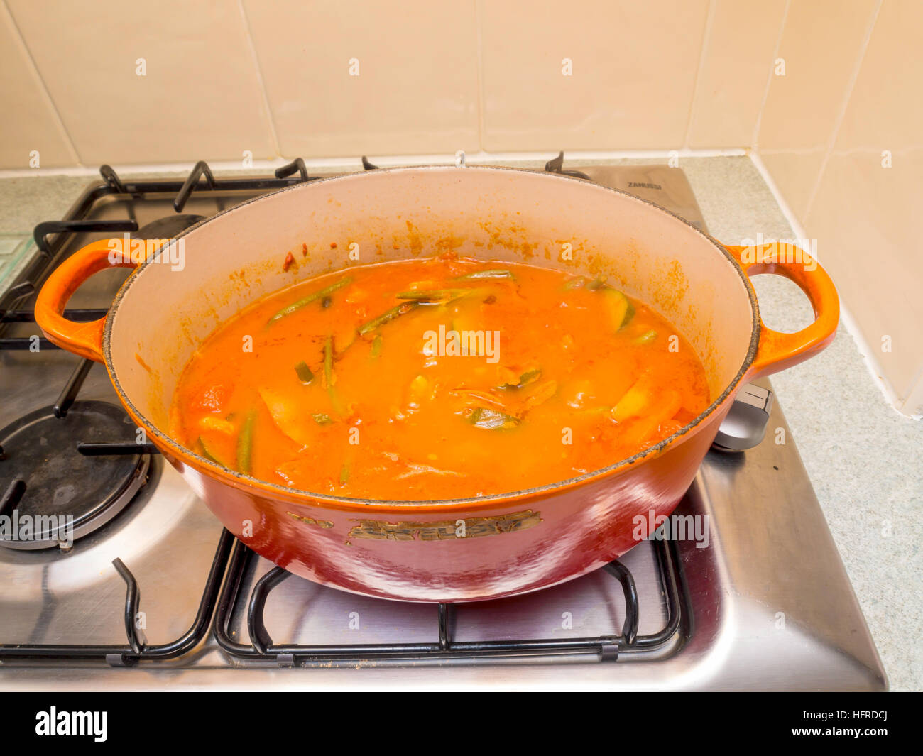 Fasolakia or Greek Bean Stew cooking in a red casserole dish on a gas