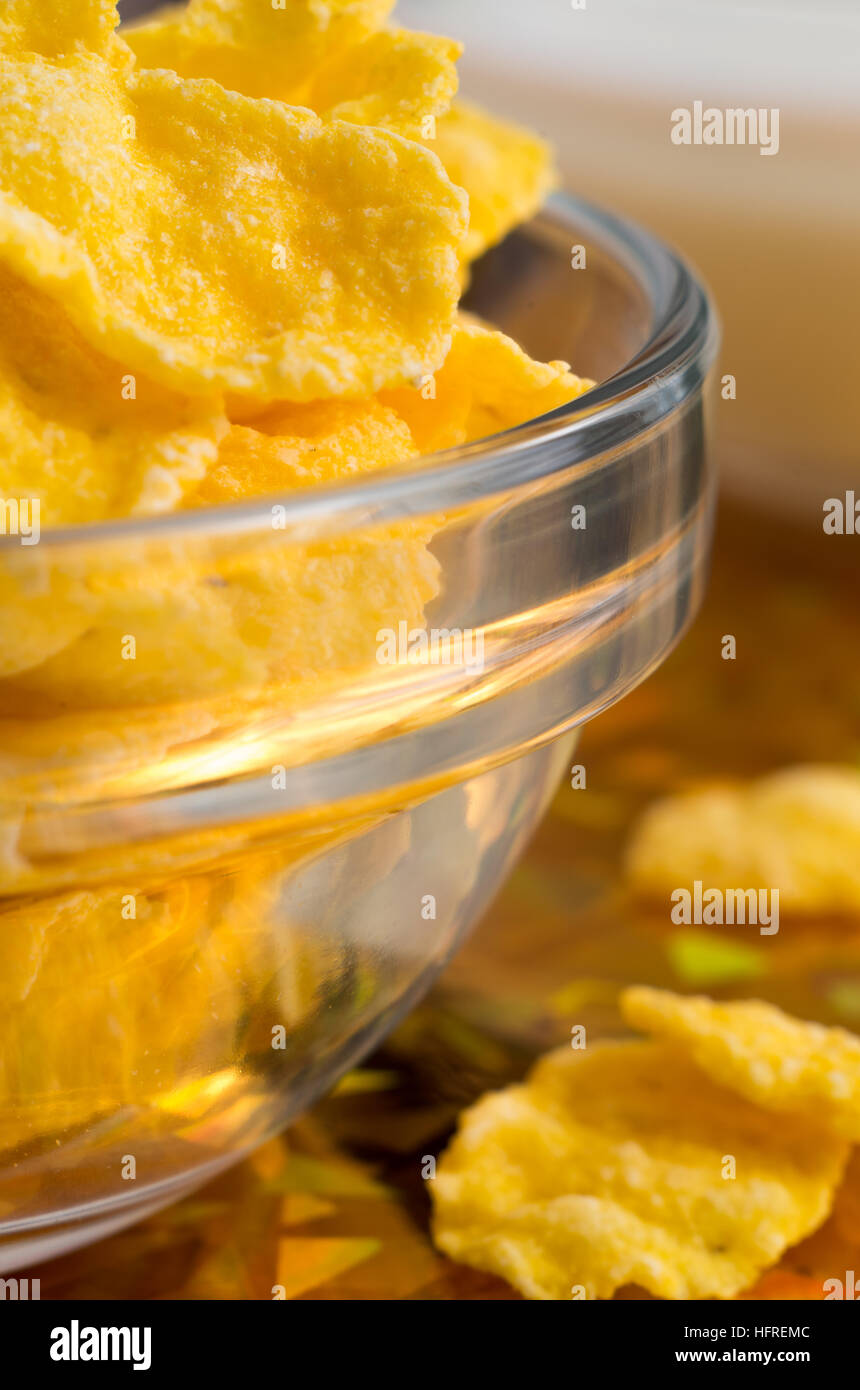 Ingredient for breakfast. Dry corn flakes in a transparent bowl closeup with blur. Stock Photo