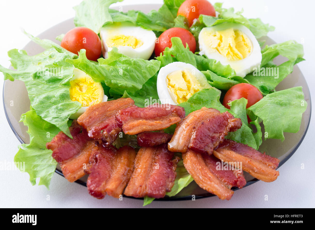 Shredded lettuce, cherry tomatoes, bacon and boiled eggs on a plate close-up with shallow depth of field Stock Photo