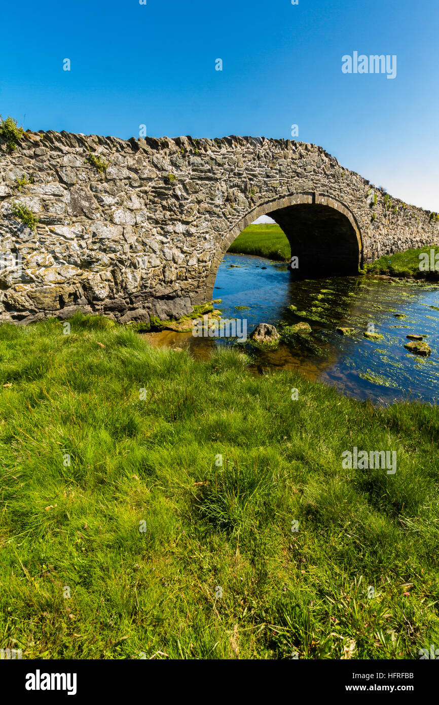 Eighteenth Century stone hump back bridge, with water channel, the river Ffraw, and blue sky. Aberffraw, Anglesey, Wales, United Kingdom, Europe Stock Photo