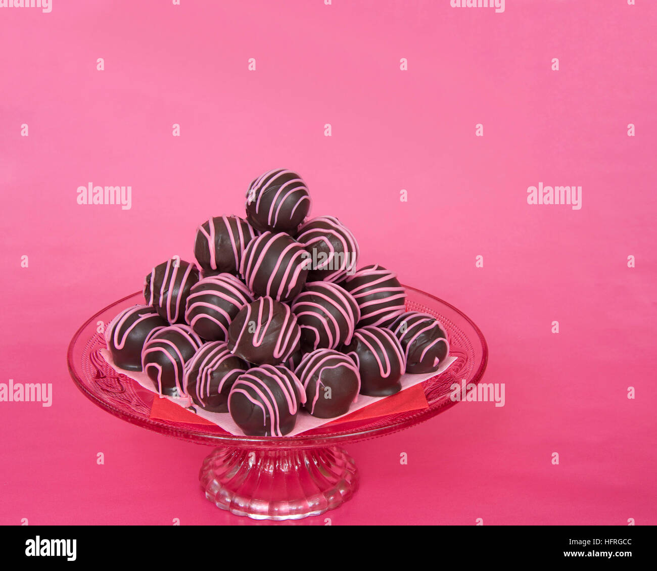 Chocolate cake balls stripped with pink candy melts stacked pyramid pattern  on a pink glass pedestal plate for Valentines Day on white doily and pink  Stock Photo - Alamy