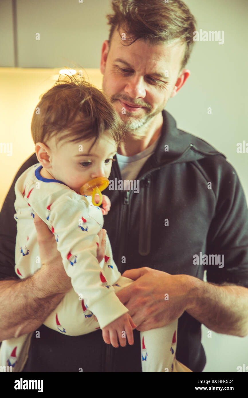 A dad holding his baby boy in his sleeper with a natural rubber soother in his mouth Stock Photo