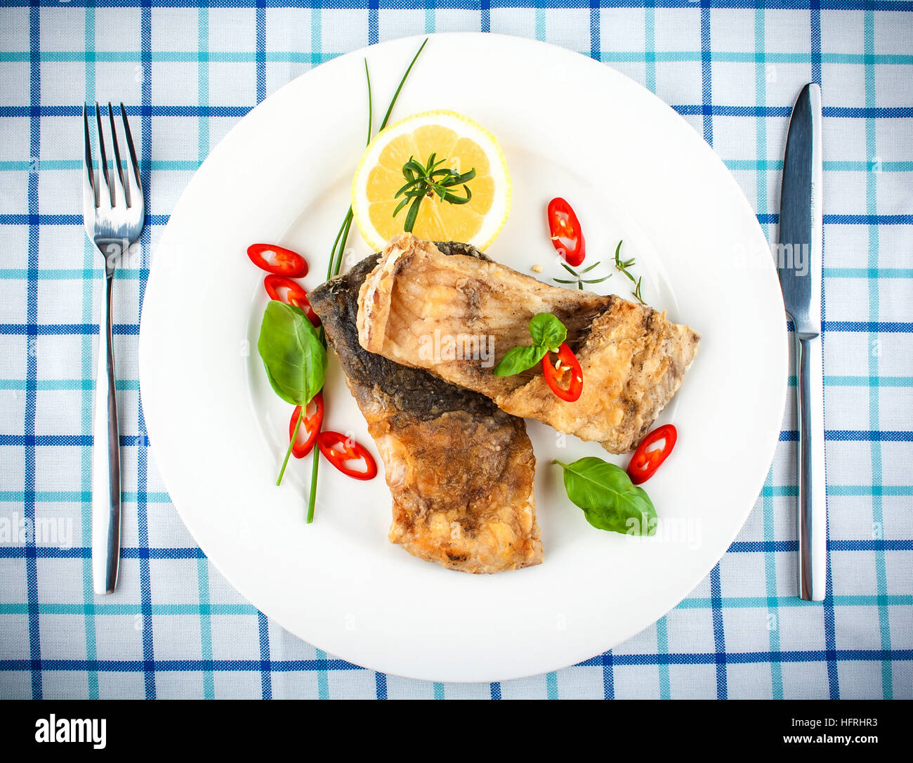 Fried fish on white plate and fork, knife, close up Stock Photo