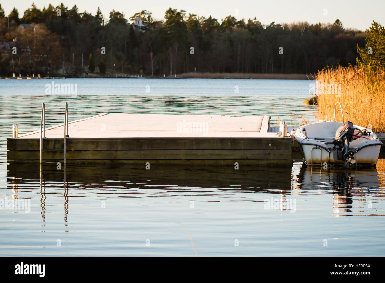 Small boat with outboard motor tied to a frost bitten floating pier in motionless water. Location Ronneby in southern Sweden. Stock Photo