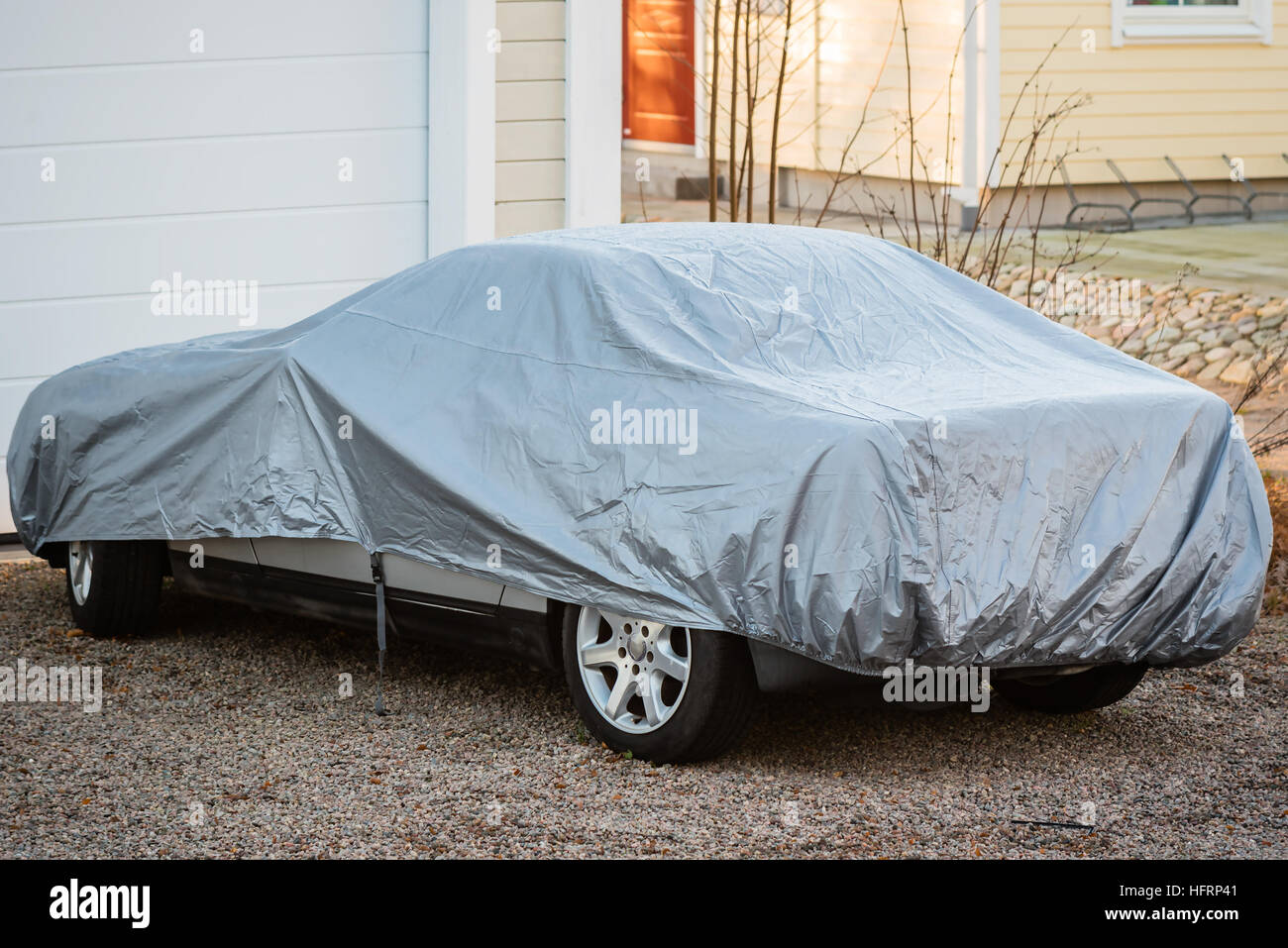 Sports car under silver colored cover outside a closed garage. Stock Photo