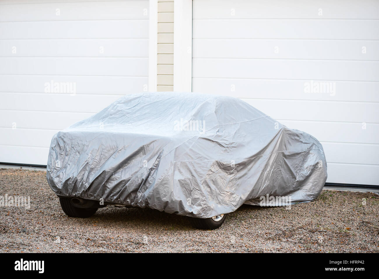 Sports car under silver colored cover outside a closed garage. Stock Photo