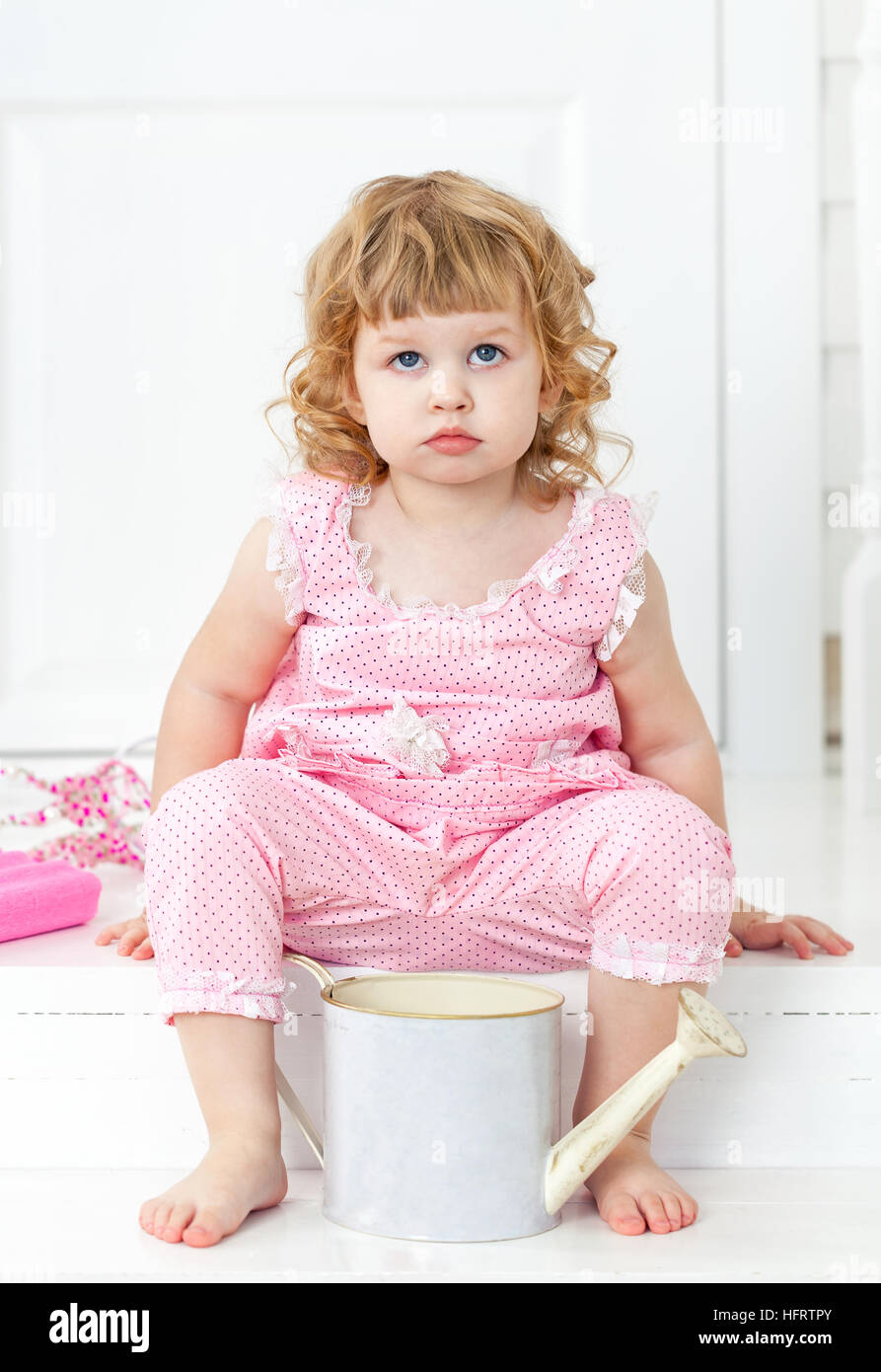 Little cute curly girl in a pink dress with polka dots sitting on the ...