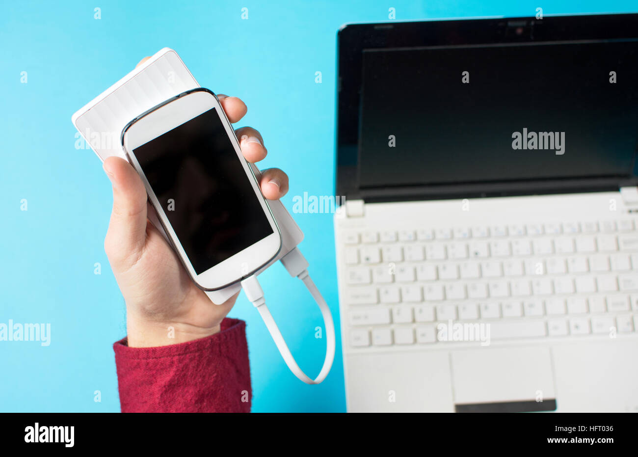 male hands holding a white cellphone connected to a power bank on blue Stock Photo