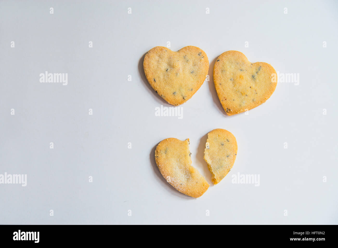 Three heart-shaped biscuits, one of them broken in two pieces. Stock Photo