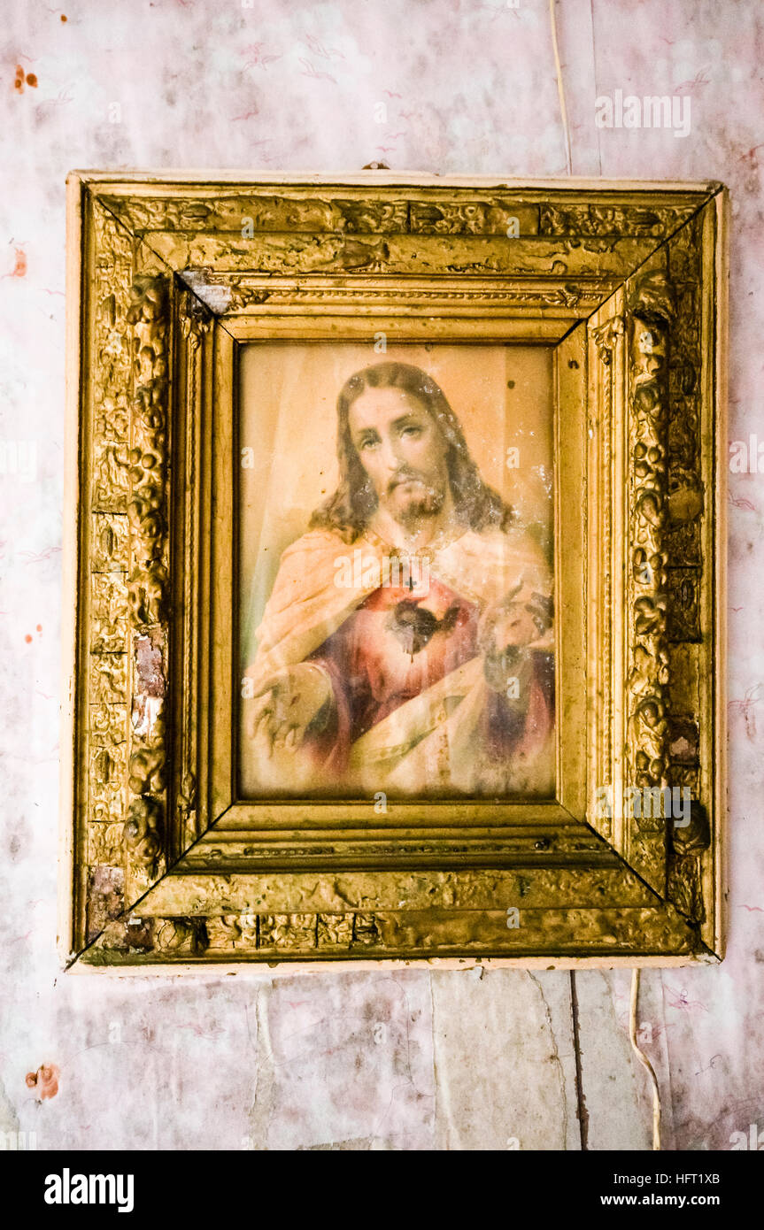 Very old Sacred Heart picture of Jesus Christ hangs on a dirty wall. Stock Photo