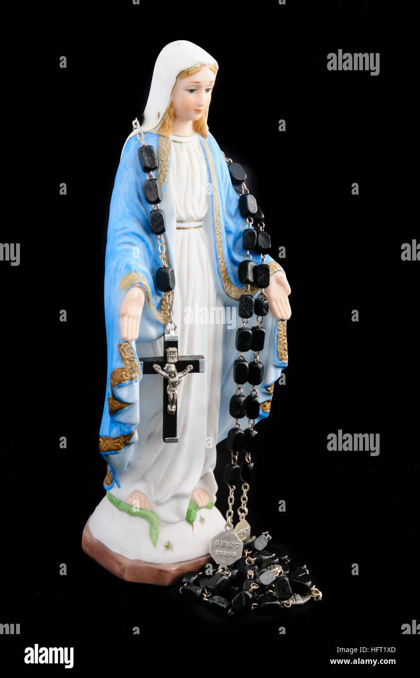 Statue of the Virgin Mary with rosary beads against black background Stock Photo