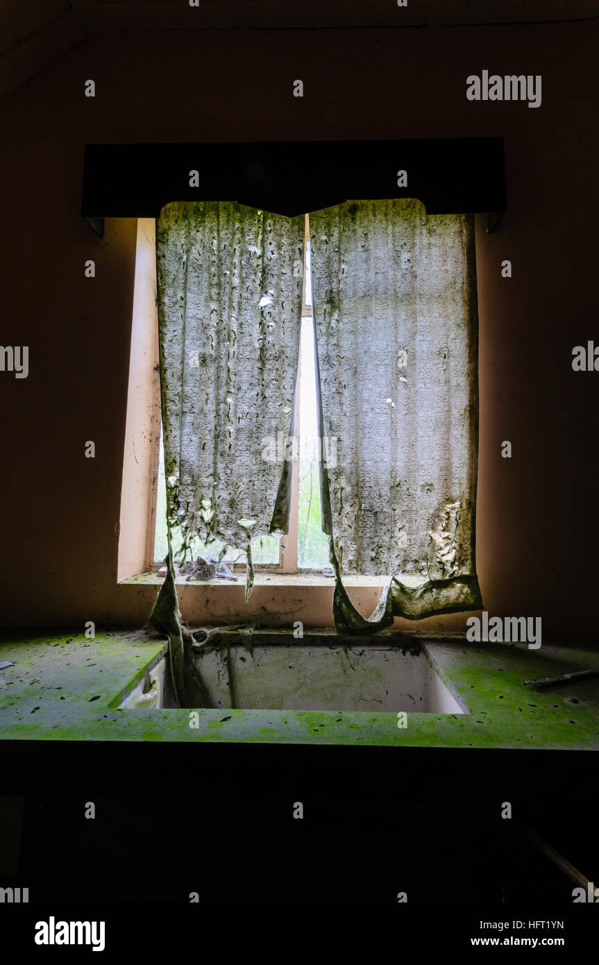 Very dirty kitchen sink and torn net curtains in an abandoned house. Stock Photo
