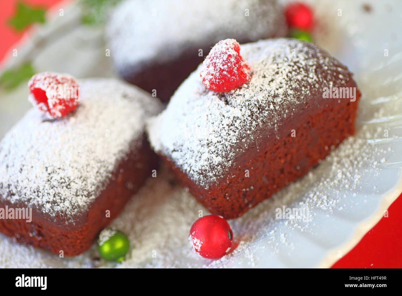 Small chocolate cakes with fresh raspberries and powdered sugar with tiny Christmas ornaments Stock Photo