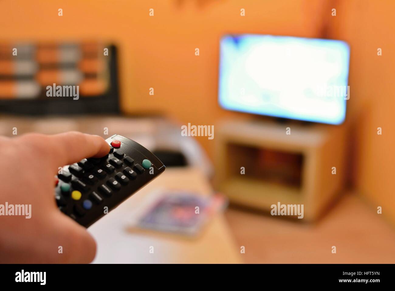 Holding the TV remote control and switching the channel on television. Stock Photo