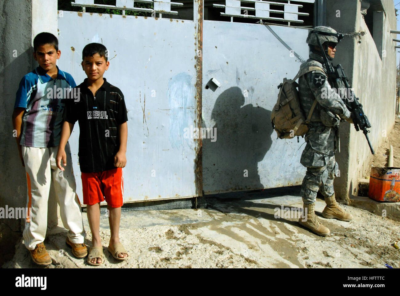 070712-N-9500T-055 KHAN BANI SA'AD, Iraq (July 12, 2007) - Two Iraqi boys watch a convoy of U.S. Army and Iraqi army vehicles drive past while Staff Sgt. Sophearak Huy keeps an eye on an alley during a mission. U.S. and Iraqi army units conducted a cordon and search mission near Khan Bani Sa'ad to clear the area of insurgents and cache sites. U.S. Navy photo by Mass Communication Specialist 2nd Class Scott Taylor (RELEASED) US Navy 070712-N-9500T-055 Two Iraqi boys watch a convoy of U.S. Army and Iraqi army vehicles drive past while Staff Sgt. Sophearak Huy keeps an eye on an alley during a mi Stock Photo