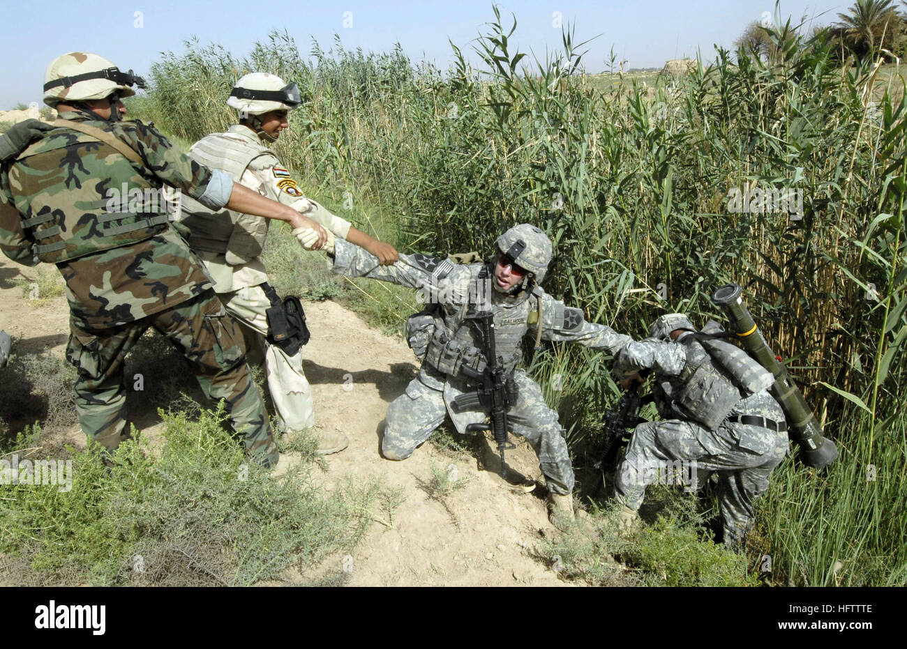 070712-N-9500T-105 KHAN BANI SA'AD, Iraq (July 12, 2007) Ð U.S. Army Sgt. Steven Calhoun is assisted by Iraqi army soldiers in pulling out a Soldier after he fell into an irrigation ditch during a joint mission.  Soldiers assigned to Alpha Battery, 2nd Battalion, 12th Infantry Regiment, 2nd Infantry Division, and units of the Iraqi army are conducting a cordon and search mission to clear the area of insurgents and cache sites. U.S. Navy photo by Mass Communication Specialist 2nd Class Scott Taylor (RELEASED) US Navy 070712-N-9500T-105 U.S. Army Sgt. Steven Calhoun is assisted by Iraqi army sol Stock Photo