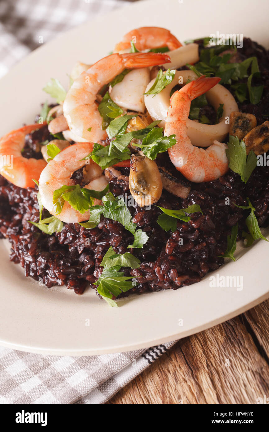 Black rice with seafood and herbs closeup on a plate. vertical Stock