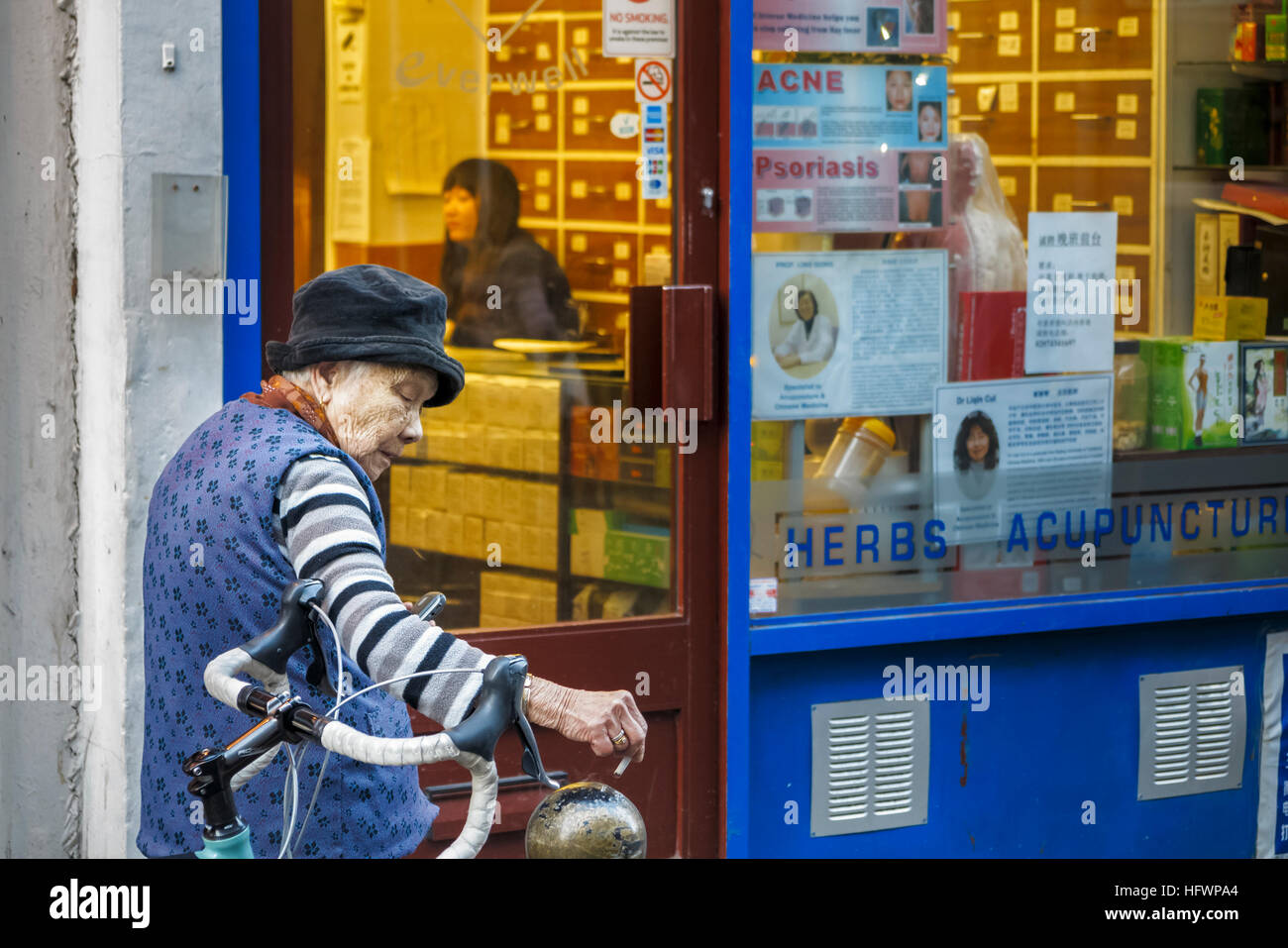 Old Chinese woman smoking a cigarette outside a Chinese medicine shop in  Chinatown, Westminster, London West End, UK Stock Photo