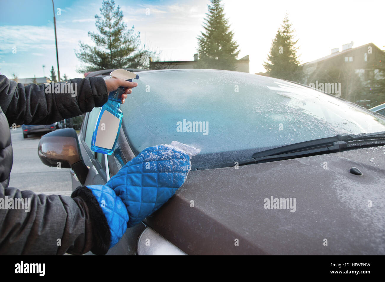 Man uses defroster spray to remove frost from the car windshield Stock Photo