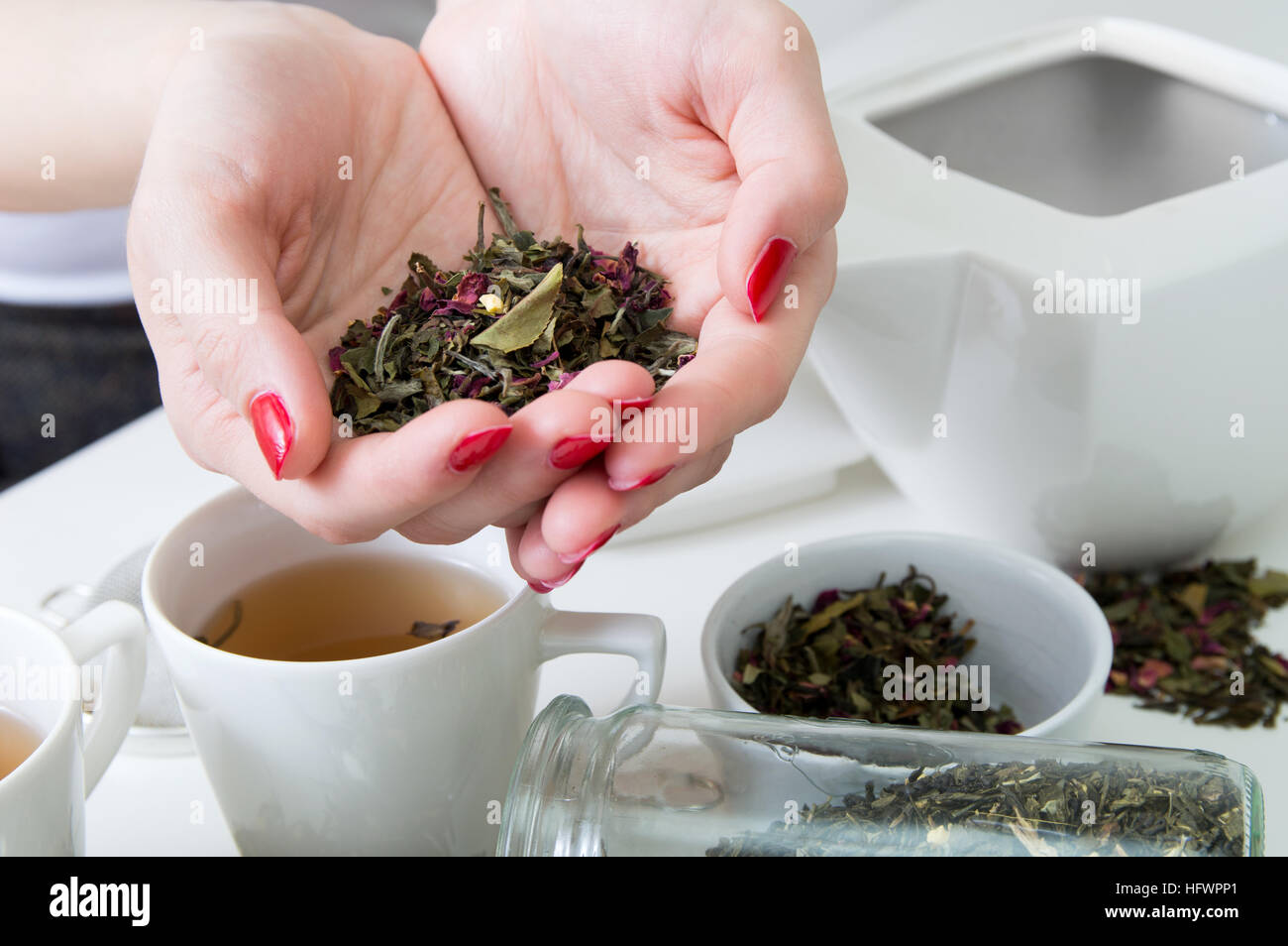 Hand Over Tea Dried green tea in woman's hands over white table with different kinds ...