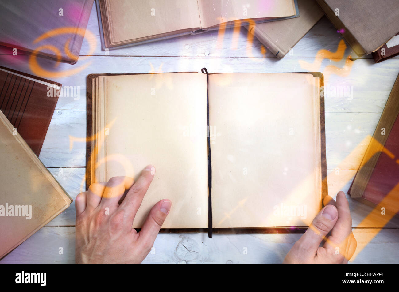 Old magic book with glowing zodiac symbols and man's hand shows important place. Empty page for your text Stock Photo