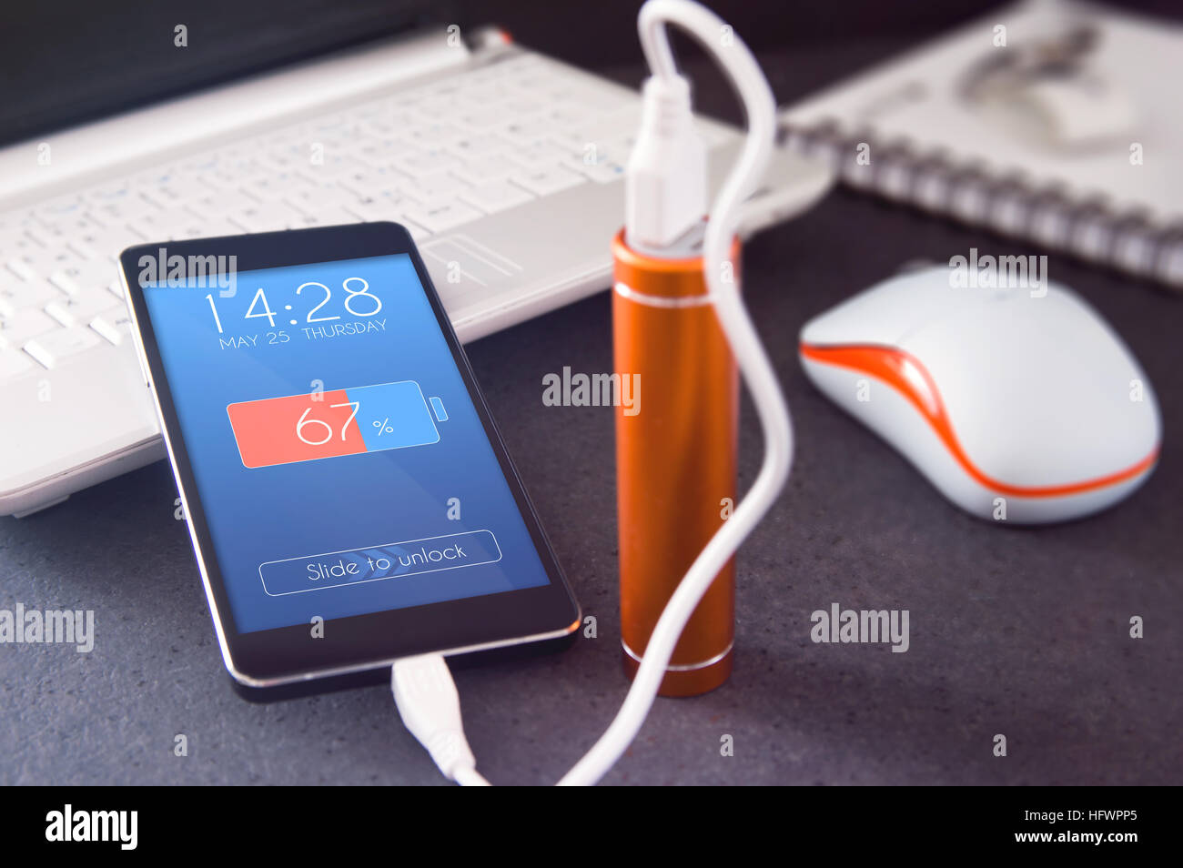 Phone charging with energy bank over the desk. Depth of field on smartphone lock screen graphically created Stock Photo