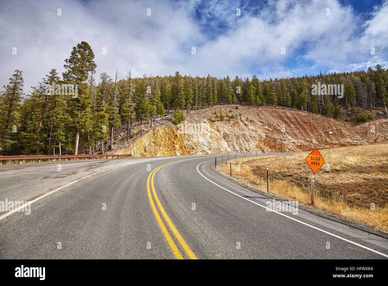 Mountain road curve with slide area warning sign. Stock Photo