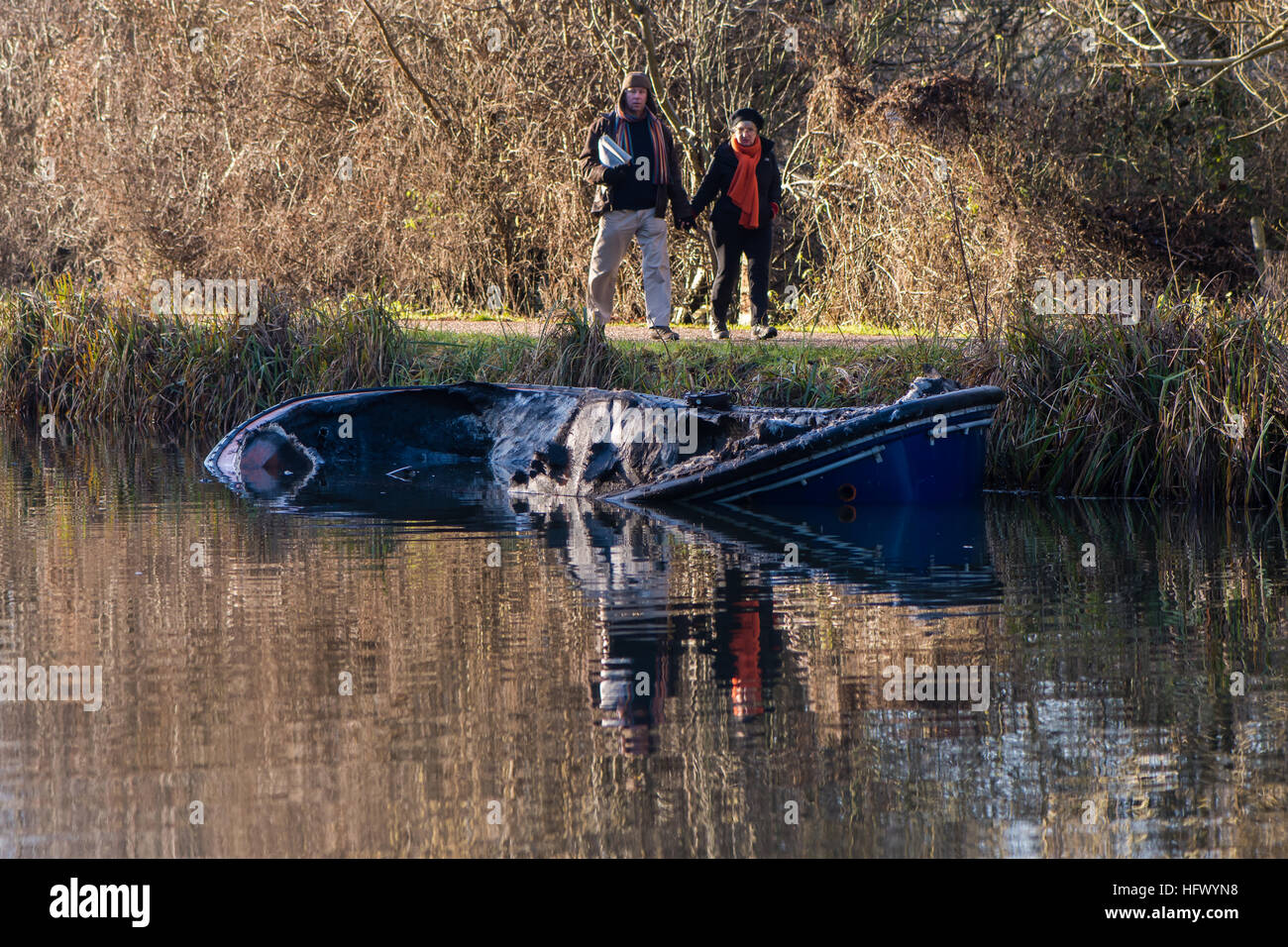 Partially submerged canal boat after fire with onlookers. Damaged hull of narrow boat in Kennet and Avon Canal after fire Stock Photo
