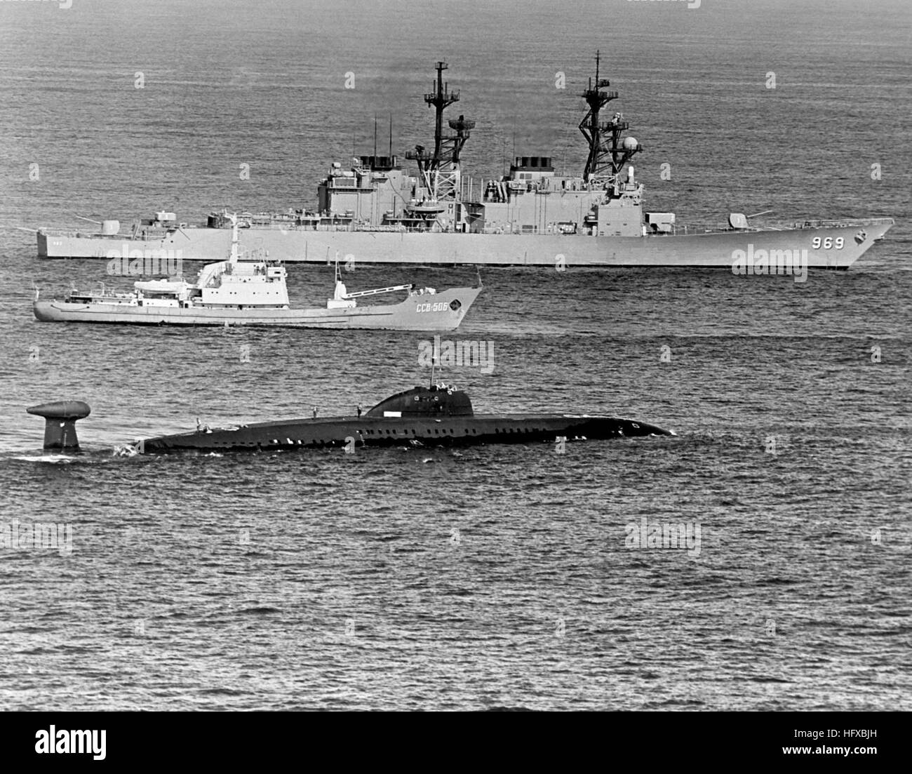 A starboard beam view of the destroyer USS PETERSON (DD-969), background, underway near a Soviet Moma Class survey ship and a disabled Victor III class submarine, foreground. USS Peterson (DD-969) with Victor class sub Stock Photo