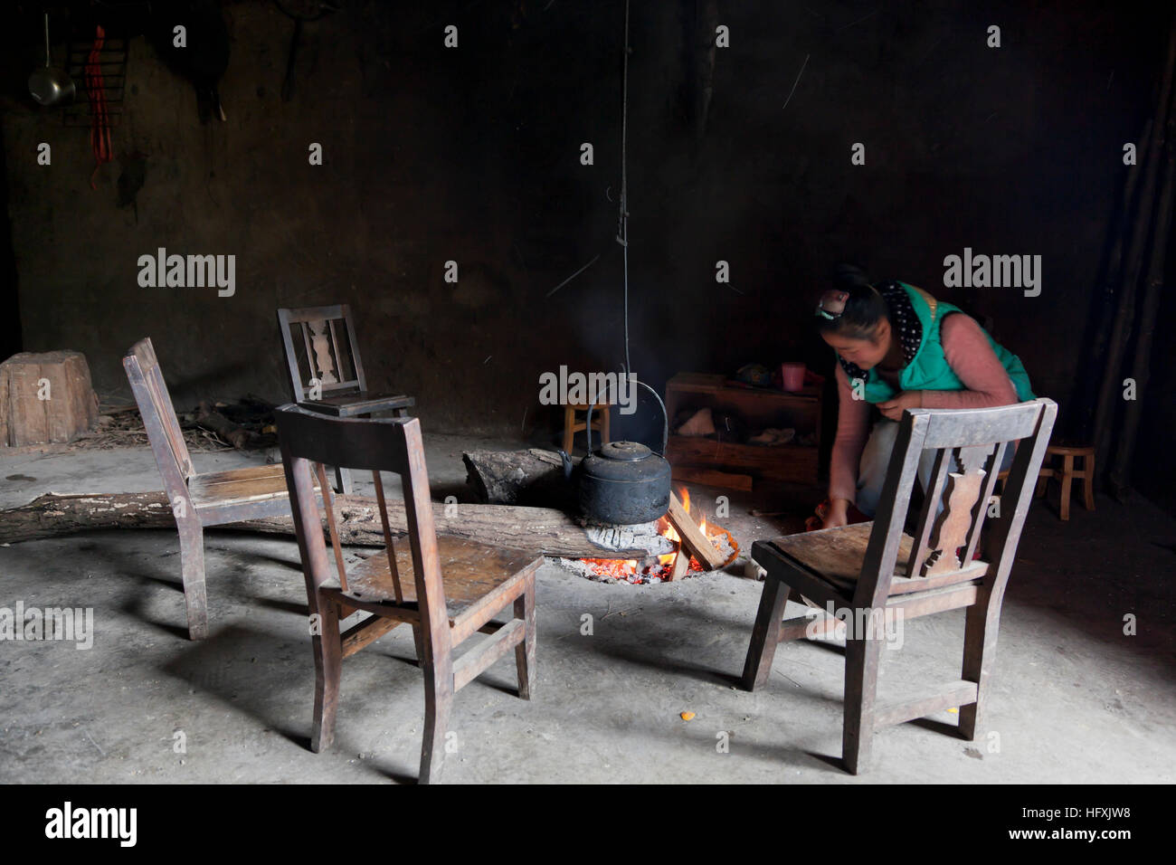 A teenage girl in a remote village in west China boils water on an open log fire in the living room of her parents' farmhouse. Stock Photo
