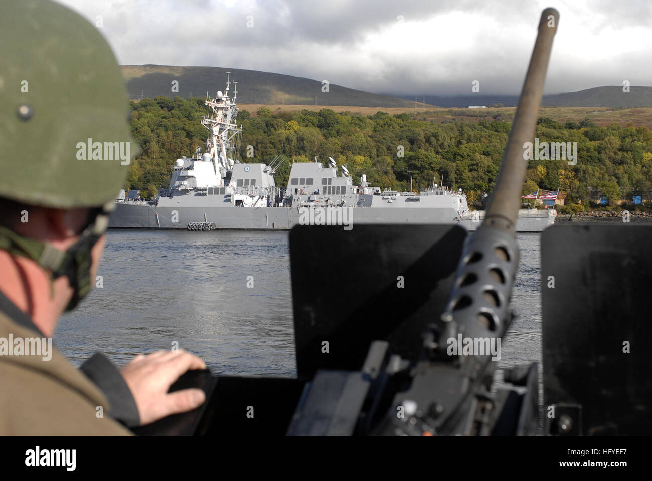 101003-N-5324W-024 FASLANE, Scotland (Oct. 3. 2010) Gunner's Mate 2nd Class Scott Wegmann stands watch at the .50-caliber machine gun mount aboard the guided-missile destroyer USS Stout (DDG 55) as the ship departs Faslane, Scotland to commence Joint Warrior 10-2. The guided-missile destroyers USS Bainbridge (DDG 96) and USS Nitze (DDG 94) are moored in the background. Joint Warrior is a multinational exercise designed to improve interoperability between allied navies and prepares participating crews to conduct combined operations during deployment. (U.S. Navy photo by Mass Communication Speci Stock Photo