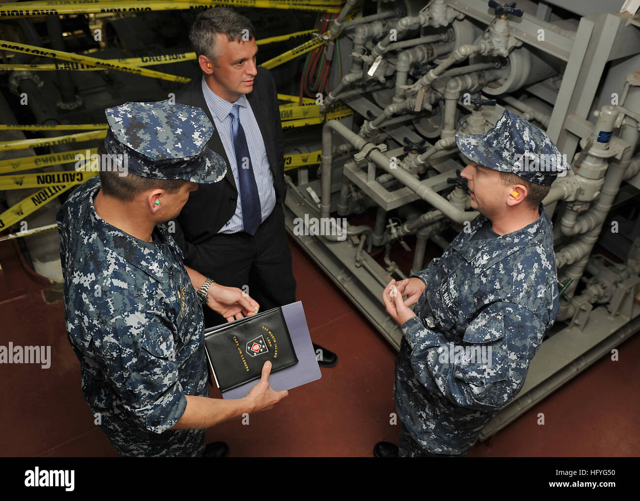 101108-N-1947A-008 SAN DIEGO (Nov. 8, 2010) Deputy Assistant Secretary of the Navy for Energy Thomas Hicks speaks with Capt. Jim Landers, commanding officer of the amphibious assault ship USS Makin Island (LHD 8), and Gas Turbine System Technician (Mechanical) 1st Class Nicholas Ayres during a tour of the shipÕs main machinery room. Makin Island, the NavyÕs first operational hybrid-electric amphibious assault ship, is expected to save the Navy $250 million throughout its 40-year life cycle. (U.S. Navy photo by Mass Communication Specialist 2nd Class Kellie Abedzadeh/Released) US Navy 101108-N- Stock Photo