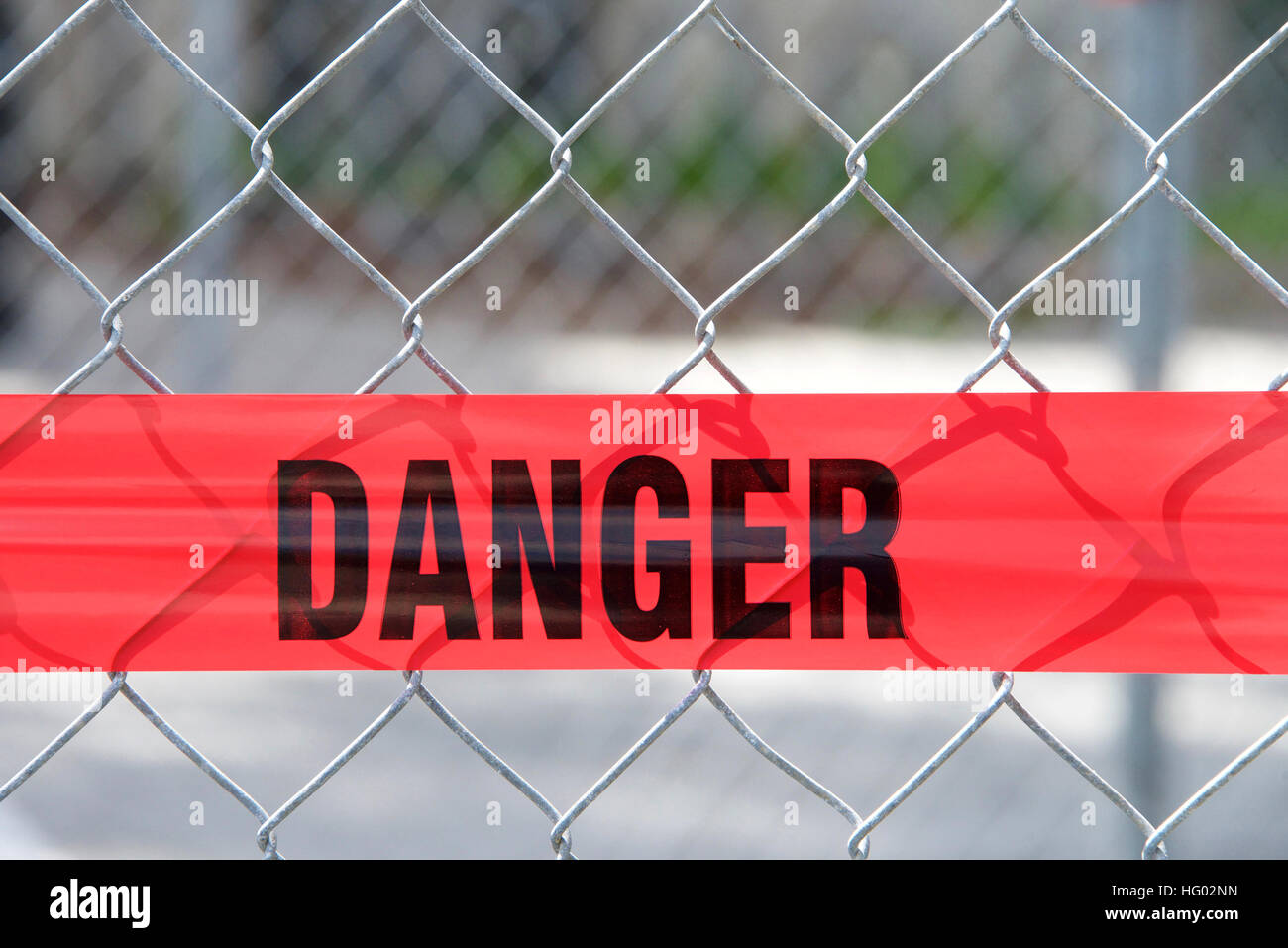 Red reflective danger barrier tape across a chain link fence to keep pedestrians out of construction zone, close up on word danger Stock Photo