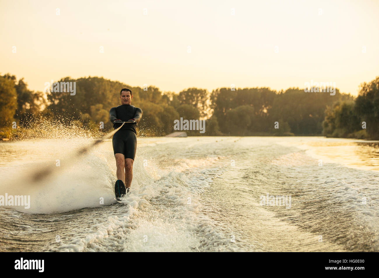 Man riding wakeboard on wave of motorboat. Male water skiing behind a boat on lake. Stock Photo